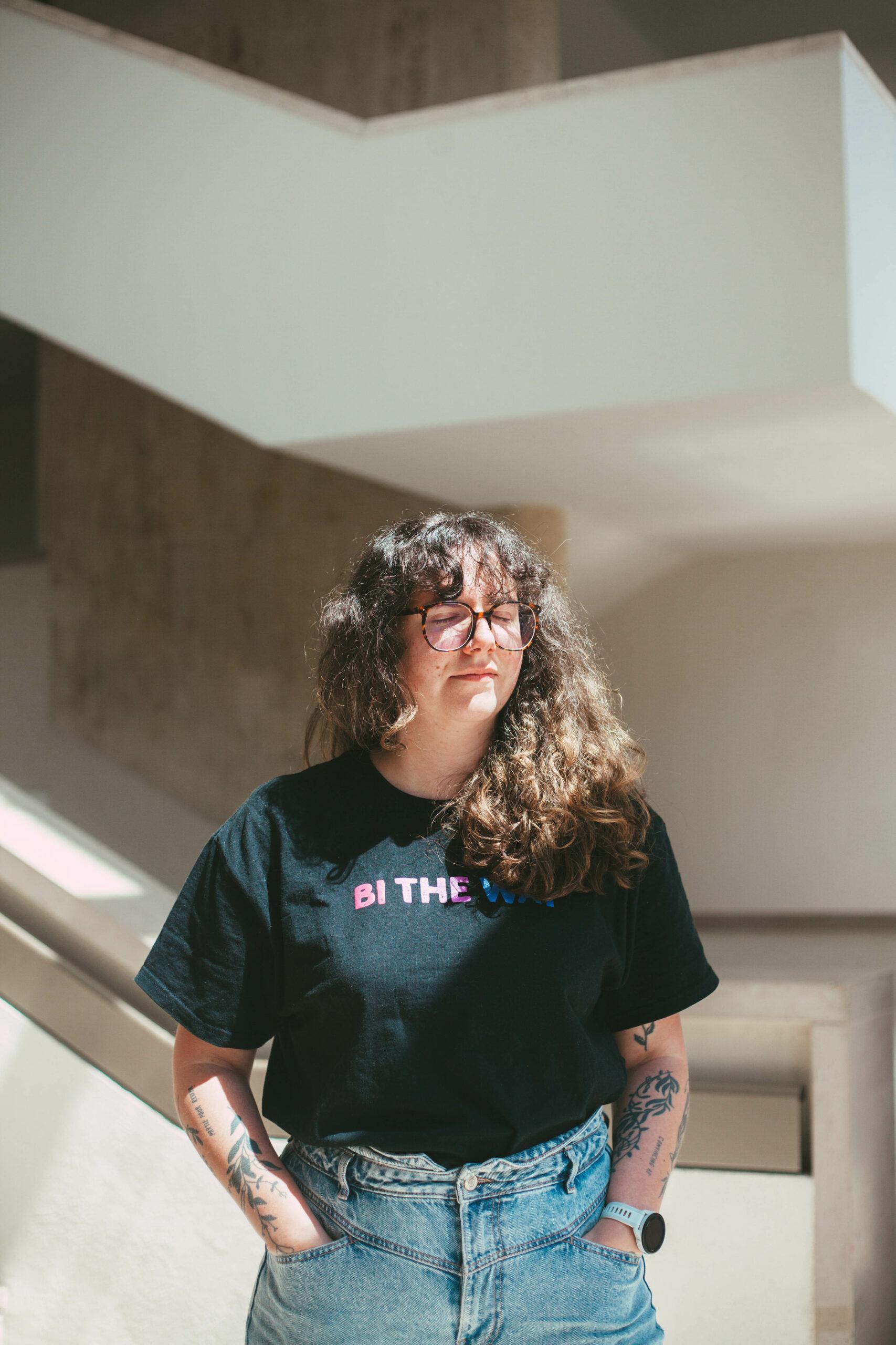 Portrait en pied de Pauline Harmange. Elle se tient debout, les yeux fermés.
Elle porte un jean et un t-shirt noir, ses cheveux longs et bouclés sont détachés.