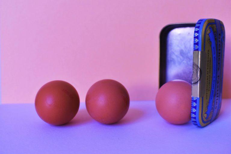 3 œufs sur une table, dont un qui semble sortir d'une petite boite métallique.